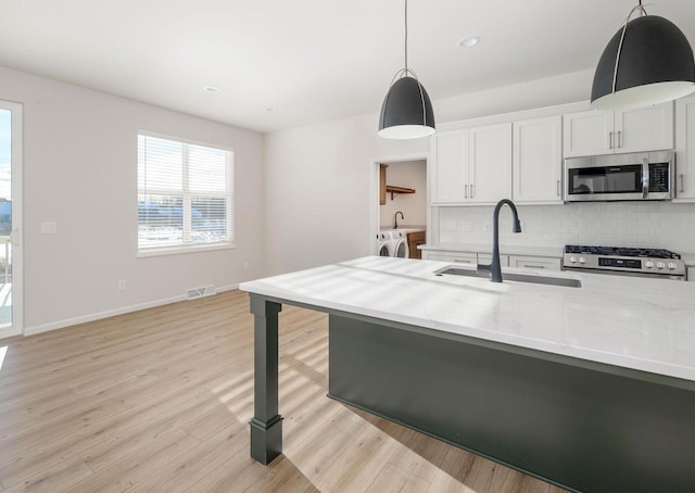 kitchen featuring appliances with stainless steel finishes, sink, white cabinets, light hardwood / wood-style floors, and hanging light fixtures