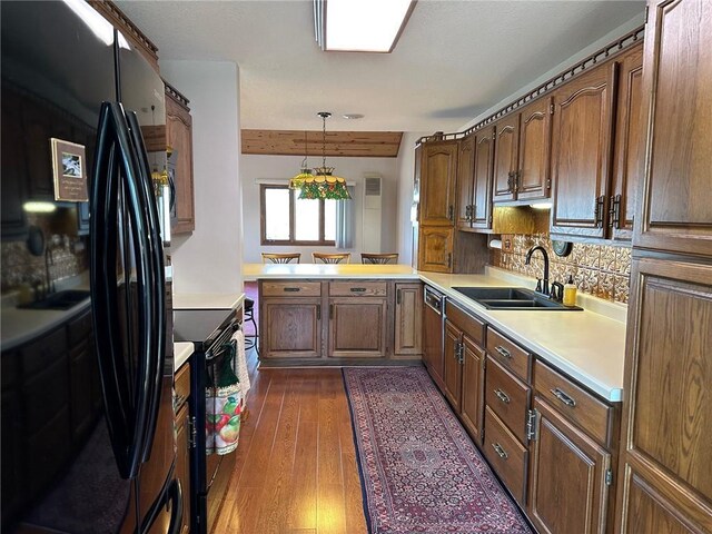 kitchen featuring dark hardwood / wood-style flooring, black appliances, pendant lighting, kitchen peninsula, and sink