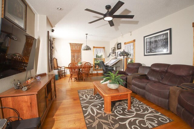 living room with ceiling fan, a textured ceiling, and light wood-type flooring