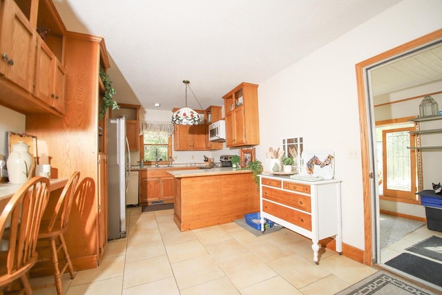 kitchen featuring kitchen peninsula, light tile patterned floors, stainless steel appliances, and decorative light fixtures