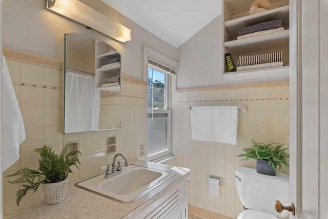 bathroom with vanity, toilet, tile patterned flooring, tile walls, and vaulted ceiling