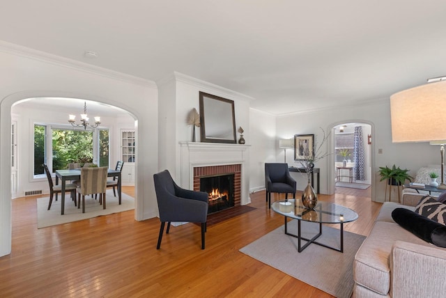 living room with wood-type flooring, ornamental molding, a fireplace, and a chandelier