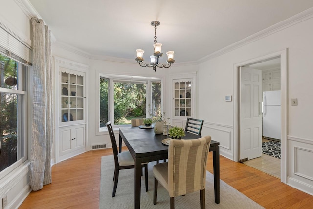 dining space featuring a healthy amount of sunlight, ornamental molding, and light hardwood / wood-style flooring