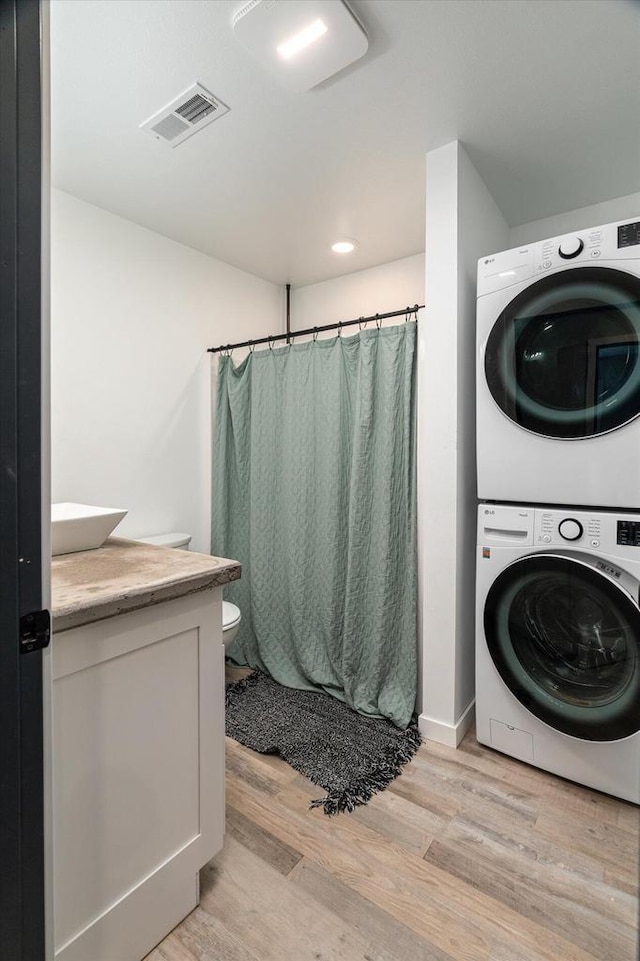 clothes washing area with visible vents, light wood-style flooring, laundry area, and stacked washer / dryer