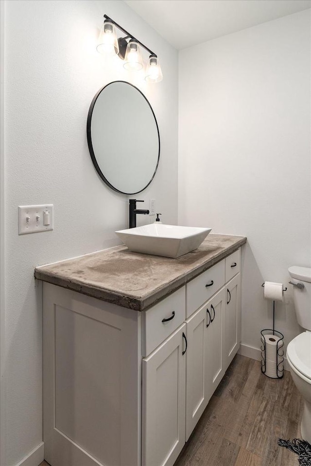 bathroom featuring baseboards, toilet, wood finished floors, and vanity