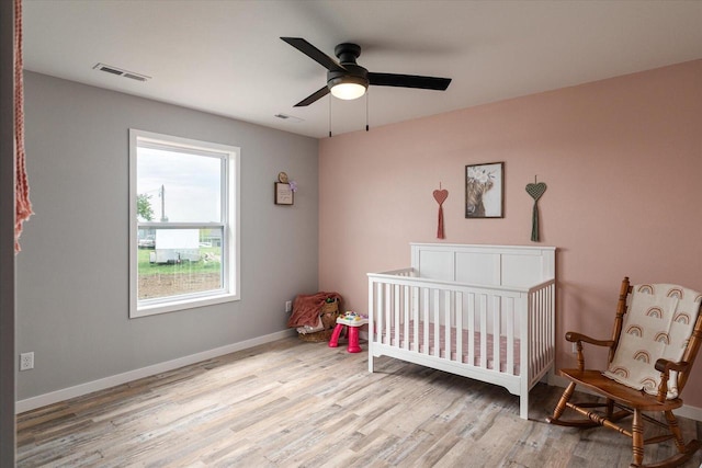 bedroom with a crib, visible vents, baseboards, and wood finished floors