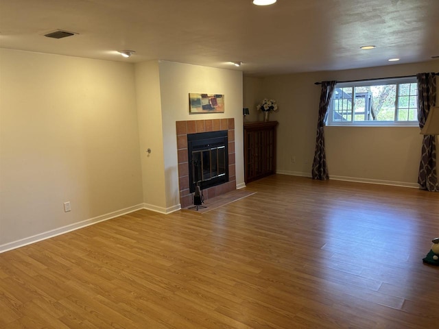 unfurnished living room with wood-type flooring and a tiled fireplace