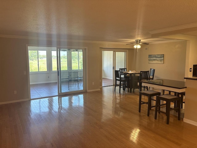 dining area featuring ceiling fan, a baseboard heating unit, hardwood / wood-style floors, ornamental molding, and a textured ceiling