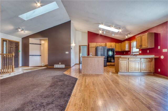 unfurnished living room with vaulted ceiling with skylight, a stone fireplace, light wood-type flooring, and a wood stove