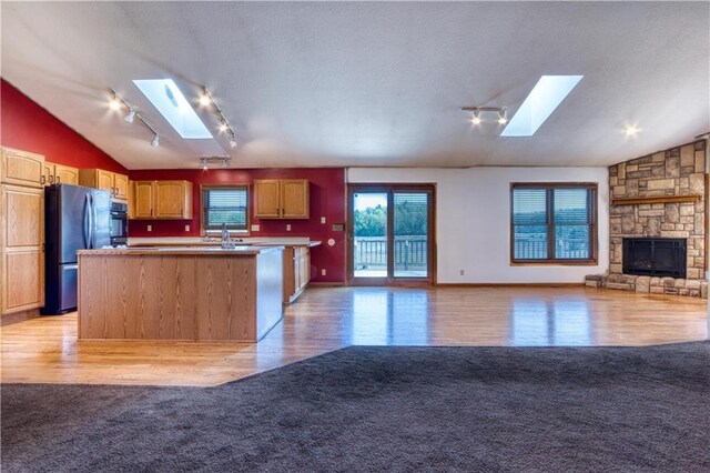 kitchen with stainless steel fridge, rail lighting, light wood-type flooring, lofted ceiling with skylight, and a center island