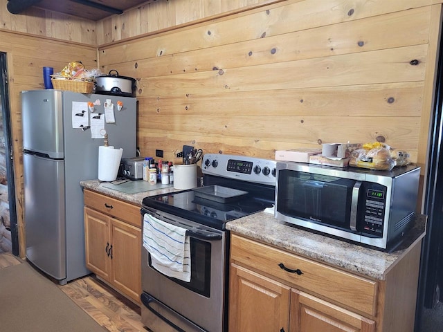 kitchen featuring light wood-type flooring, wood walls, and stainless steel appliances