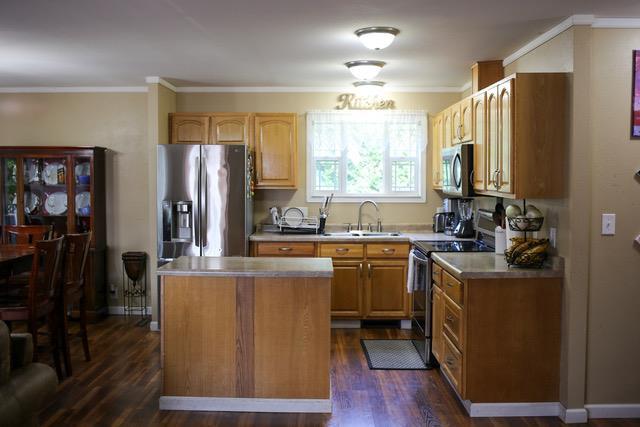 kitchen with stainless steel appliances, sink, dark wood-type flooring, a kitchen island, and ornamental molding