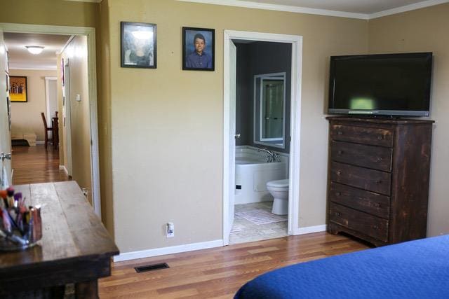 bedroom featuring wood-type flooring, crown molding, and ensuite bath