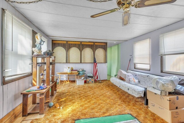 interior space featuring carpet floors, ceiling fan, and wooden walls