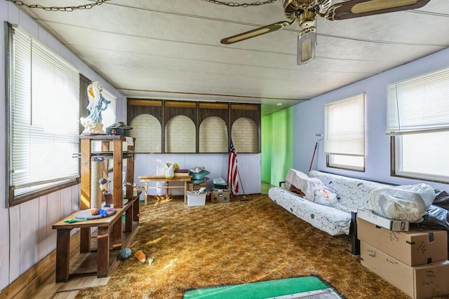 interior space with ceiling fan, wooden walls, and carpet