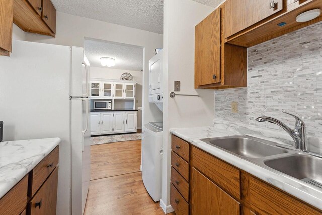 kitchen featuring white fridge, tasteful backsplash, light hardwood / wood-style floors, sink, and stainless steel microwave