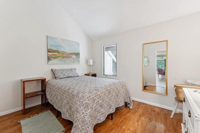 bedroom with lofted ceiling, hardwood / wood-style flooring, and a textured ceiling