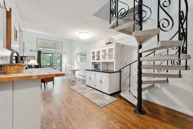 kitchen featuring light wood-type flooring, white cabinetry, a textured ceiling, wooden counters, and a baseboard radiator