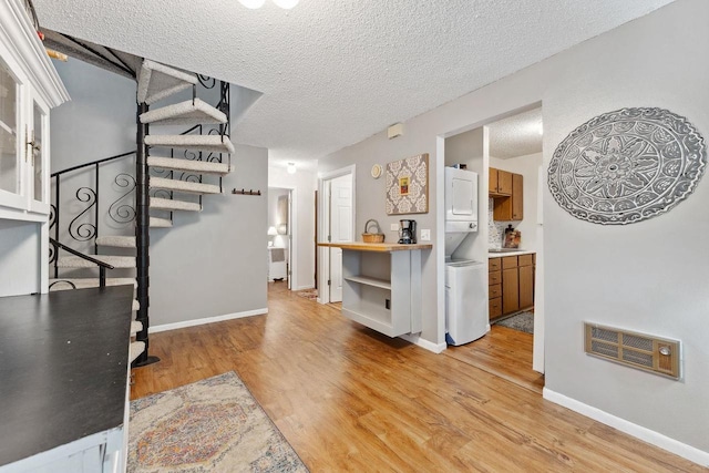 interior space with stacked washer / dryer, a textured ceiling, and light hardwood / wood-style flooring