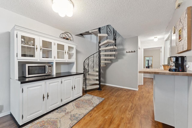 kitchen with a textured ceiling, white cabinetry, and light hardwood / wood-style floors