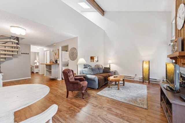 living room with a textured ceiling, hardwood / wood-style flooring, a baseboard heating unit, and vaulted ceiling with beams