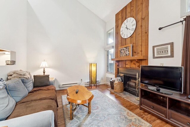 living room featuring baseboard heating, high vaulted ceiling, and light hardwood / wood-style flooring