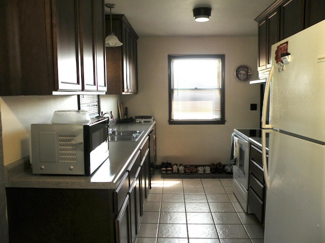 kitchen featuring decorative light fixtures, white appliances, dark brown cabinets, sink, and light tile patterned flooring