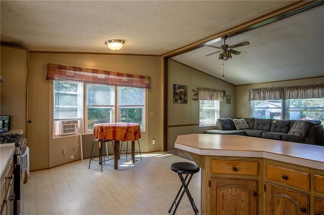 kitchen with a textured ceiling, a breakfast bar area, vaulted ceiling, stainless steel range with gas stovetop, and ceiling fan