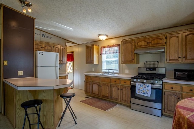 kitchen featuring gas stove, sink, lofted ceiling, a kitchen bar, and white fridge