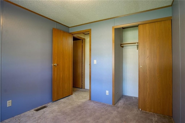 unfurnished bedroom with light colored carpet, a textured ceiling, a closet, and crown molding