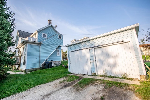 rear view of house featuring a balcony, a lawn, and a garage