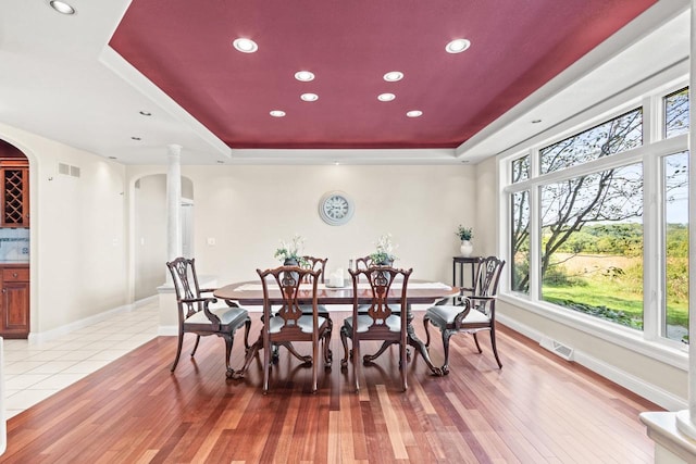 dining area with light wood-type flooring and a raised ceiling