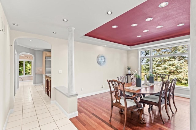 dining area with light wood-type flooring, a tray ceiling, decorative columns, and a healthy amount of sunlight