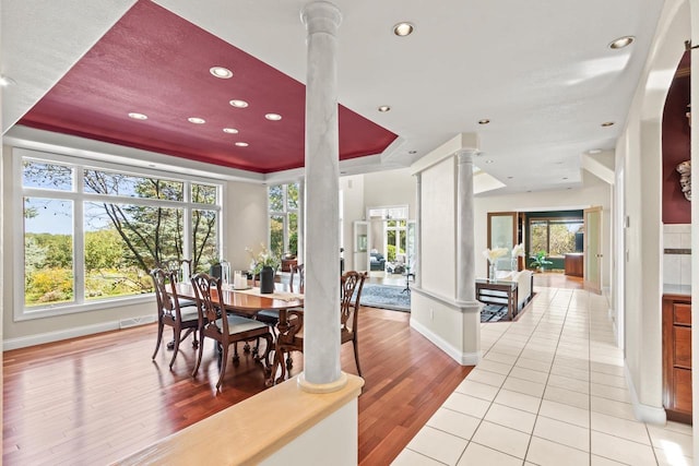 dining space with light hardwood / wood-style floors, decorative columns, and a tray ceiling