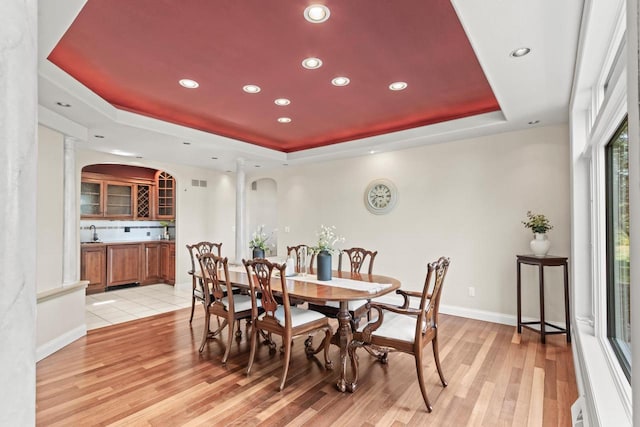 dining room with sink, light wood-type flooring, and a raised ceiling