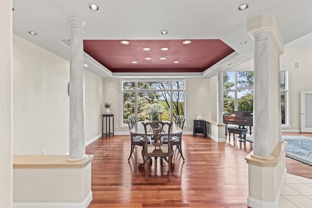 dining area with a tray ceiling, hardwood / wood-style flooring, and ornate columns