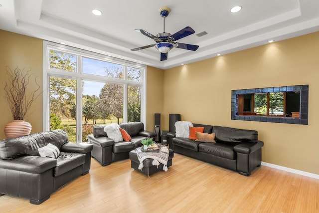 living room featuring light hardwood / wood-style flooring, ceiling fan, and a raised ceiling