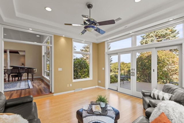 living room featuring a tray ceiling, ceiling fan, light hardwood / wood-style flooring, and french doors