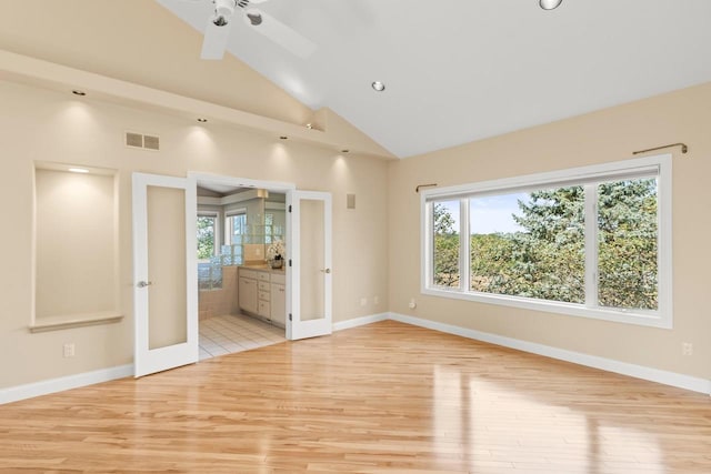 empty room with light hardwood / wood-style floors, ceiling fan, french doors, and high vaulted ceiling