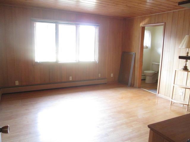 spare room with wooden ceiling, light hardwood / wood-style flooring, a baseboard radiator, and wooden walls