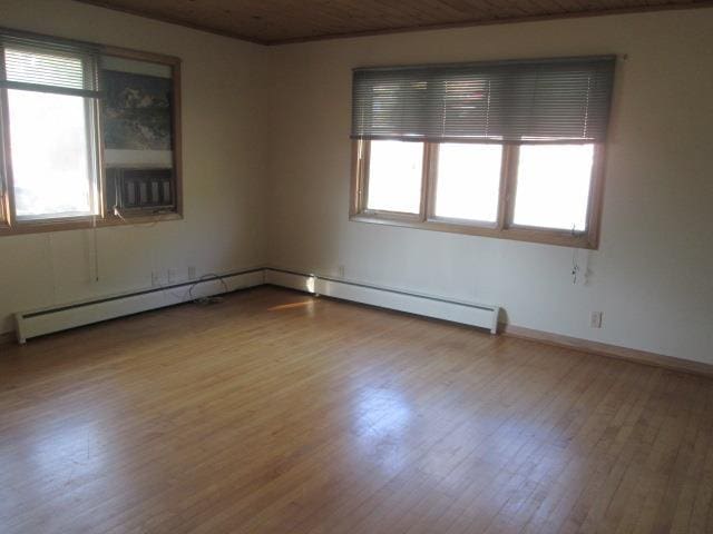 unfurnished room with hardwood / wood-style flooring, a healthy amount of sunlight, and a baseboard radiator