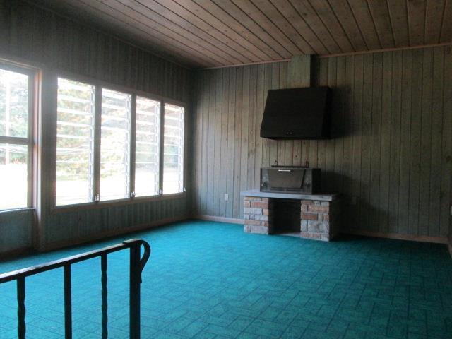 unfurnished living room with wood ceiling, wood walls, and a stone fireplace