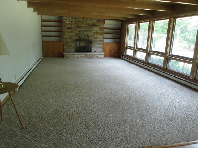 unfurnished living room featuring a stone fireplace, a baseboard radiator, beamed ceiling, and a healthy amount of sunlight