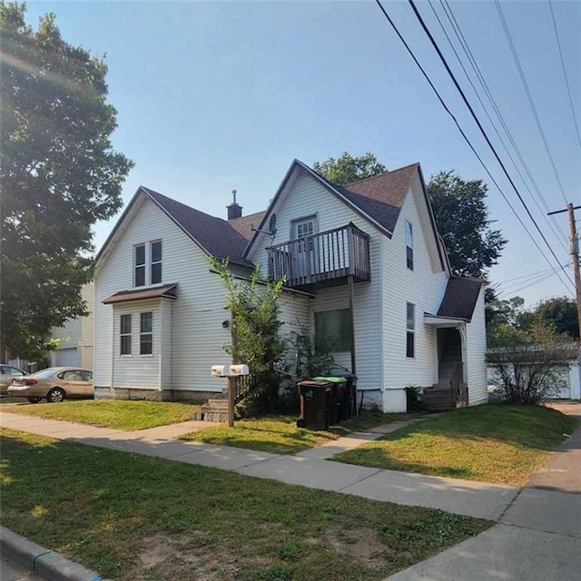 view of front of house with a balcony, a front lawn, and roof with shingles