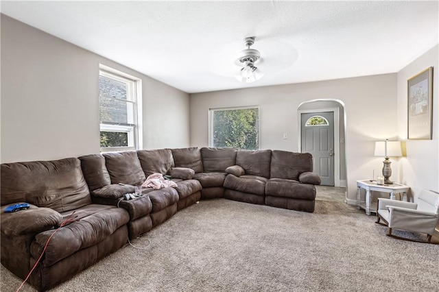 living area with a ceiling fan, plenty of natural light, arched walkways, and carpet