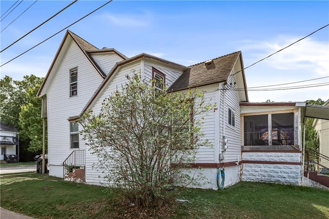 view of side of property featuring a sunroom, a shingled roof, and a yard