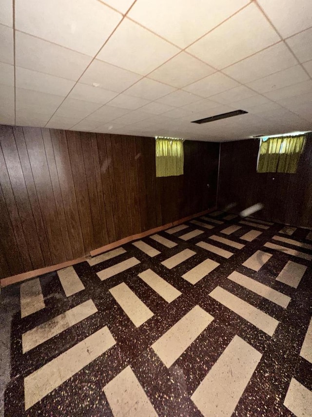 basement with wood walls and a paneled ceiling