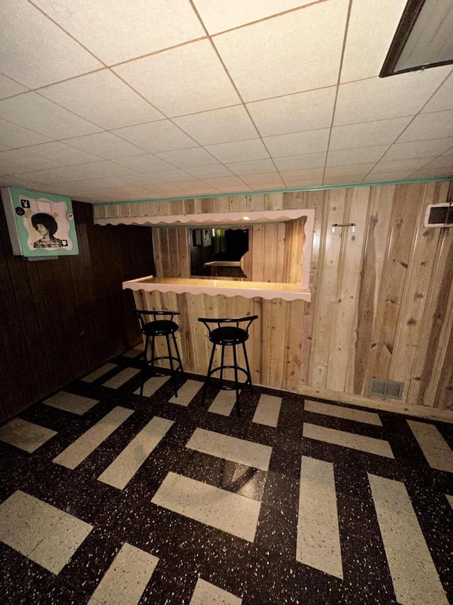 basement featuring a drop ceiling, wooden walls, and bar