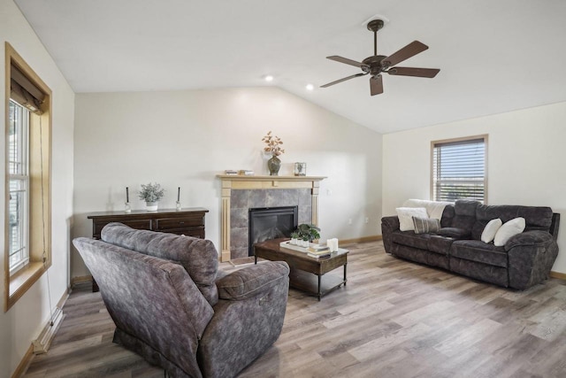 living room featuring wood-type flooring, vaulted ceiling, ceiling fan, and a tile fireplace