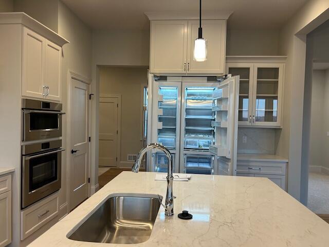 kitchen with pendant lighting, light stone countertops, sink, and double oven